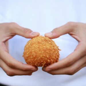 man about to break arancini ball in half using his hands, he is wearing and chefs coat