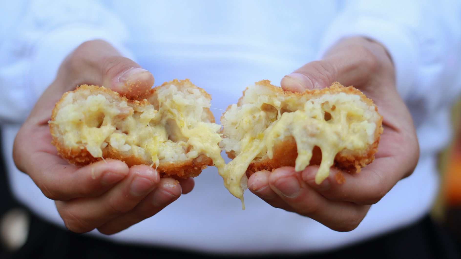 an arancini ball being pulled apart, cheesy filling oozing out