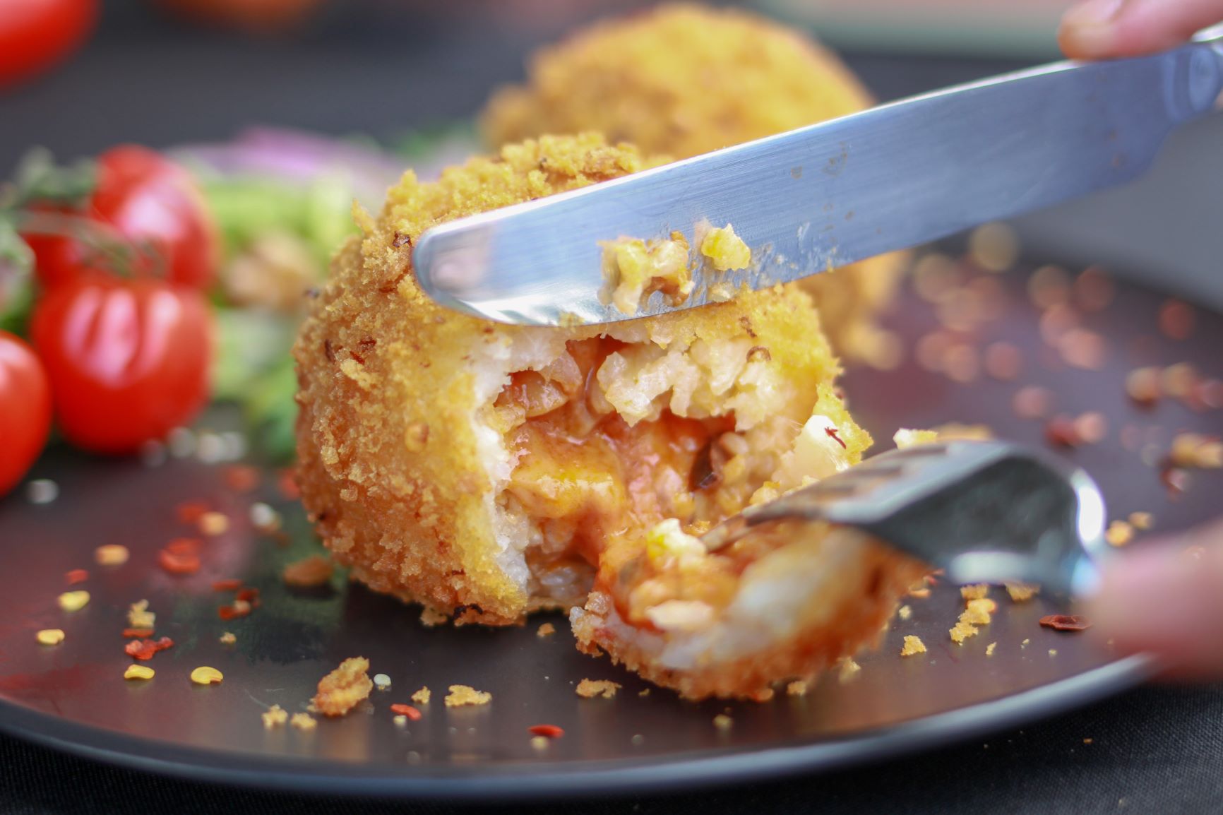 a person cutting into arancini with a knife and fork